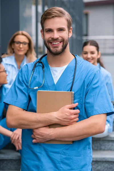 Красивый белый студент-медик, стоящий с блокнотом и смотрящий в камеру — стоковое фото