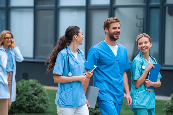 Estudiantes de medicina sonrientes y conferenciante caminando por la calle cerca de la universidad - foto de stock