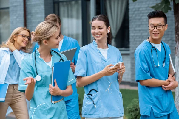 Happy multicultural students talking while walking on street near medical university — Stock Photo