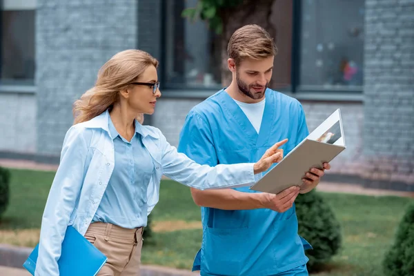 Teacher of medical university pointing on something in notebook to student on street — Stock Photo