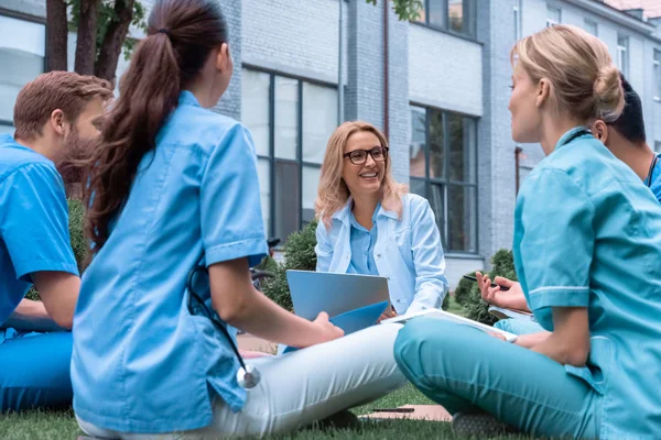 Professeur souriant ayant des leçons avec les étudiants de l'université de médecine sur herbe verte — Photo de stock