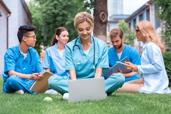 Profesor y estudiantes multiétnicos que estudian al aire libre con aparatos en la universidad médica - foto de stock