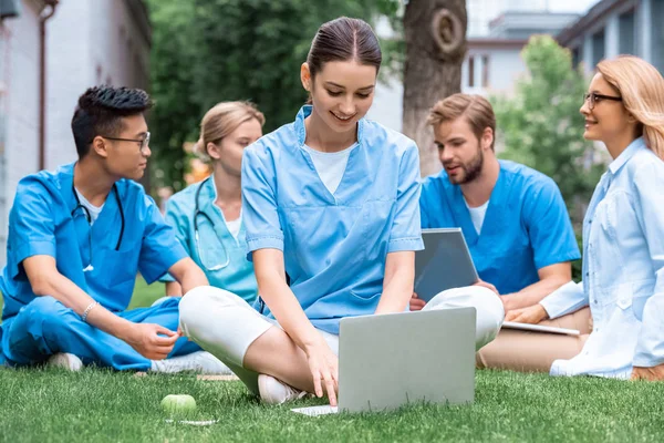 Profesor alegre y estudiantes multiculturales que estudian al aire libre con aparatos en la universidad médica - foto de stock