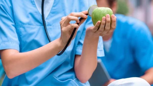 Immagine ritagliata di studente di medicina esaminando mela con stetoscopio — Foto stock