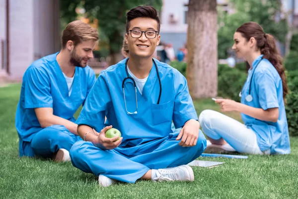 Schöner asiatischer Medizinstudent hält Apfel und schaut in die Kamera — Stockfoto