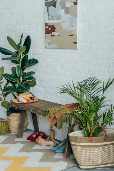 Verschiedene Schuhe unter Holzbank im Hausflur, Topfpflanze im Korb — Stockfoto