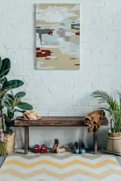 Sapatos diferentes sob banco de madeira no corredor em casa, pintura na parede — Fotografia de Stock