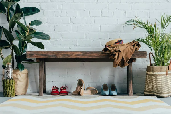 Différentes chaussures sous banc en bois dans le couloir à la maison, palmier en pot et ficus sur le sol — Photo de stock