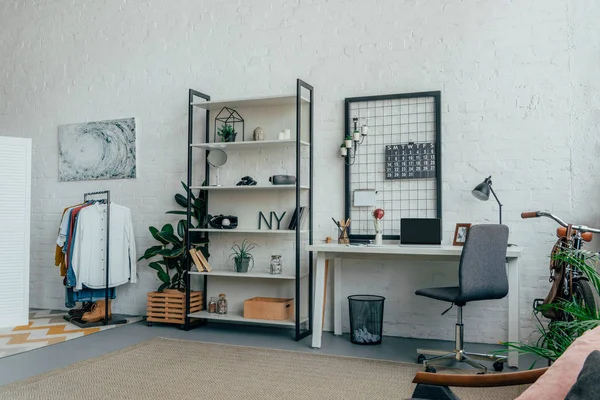 Interior de la moderna sala de estar con ordenador portátil en la mesa y ropa en perchas - foto de stock