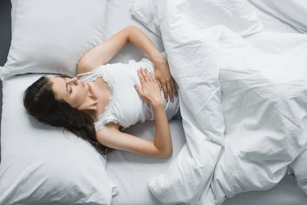 Vista superior da mulher jovem que sofre de dor abdominal enquanto deitada na cama — Fotografia de Stock