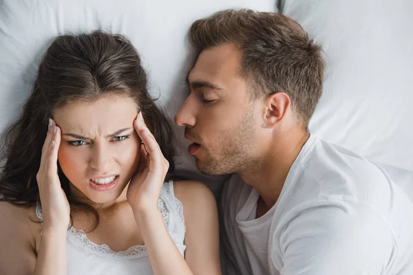 Junge wütende Frau hat Kopfschmerzen, während sie mit schnarchendem Mann im Bett liegt — Stockfoto