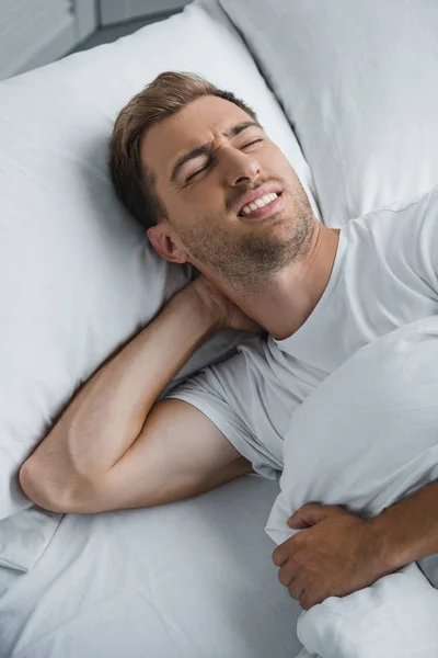 Young man lying in bed and suffering from pain in neck — Stock Photo