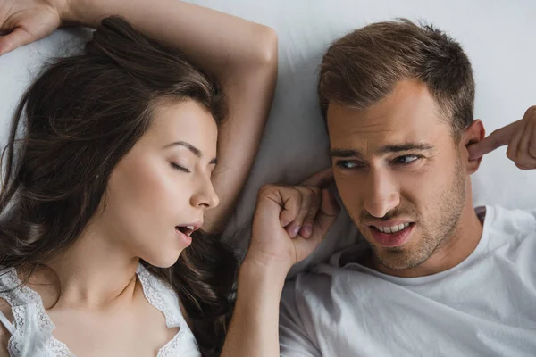 Top view of man closing ears and looking at snoring wife in bed — Stock Photo