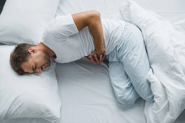 Top view of man lying in bed and suffering from stomach pain — Stock Photo