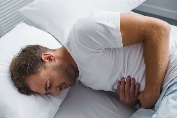 High angle view of man lying in bed and suffering from stomach pain — Stock Photo