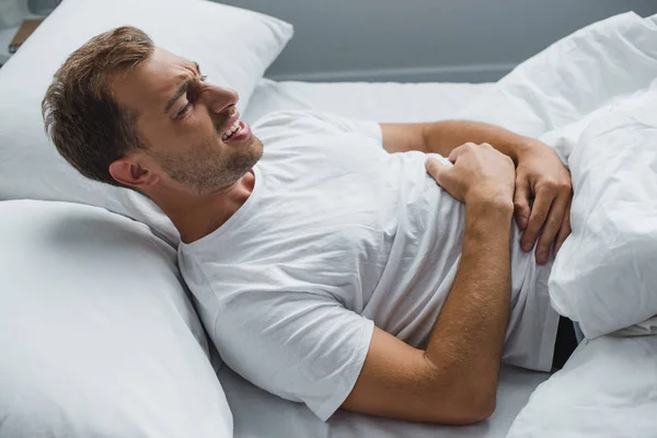 Vista de ángulo alto del hombre acostado en la cama y que sufre de dolor de estómago - foto de stock