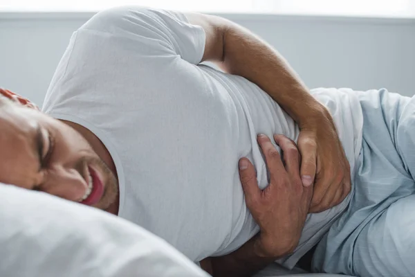 Recortado disparo de hombre que sufre de dolor de estómago en la cama - foto de stock