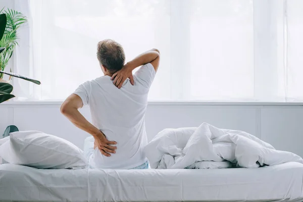 Вид сзади человека, сидящего на кровати и страдающего от боли в спине — стоковое фото