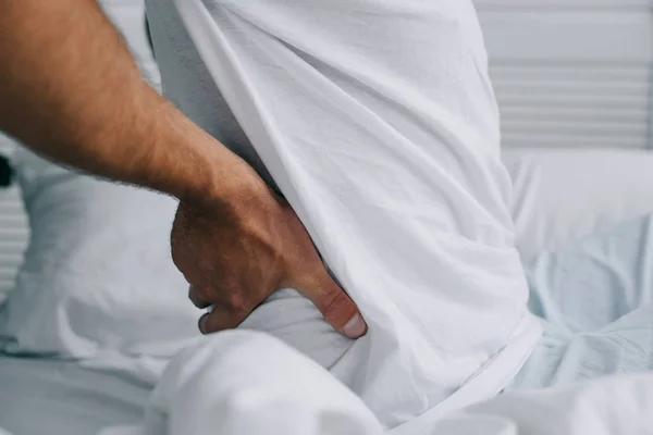 Cropped shot of man suffering from back pain in bed — Stock Photo