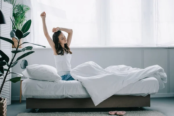 Schöne junge brünette Frau dehnt sich morgens auf dem Bett — Stockfoto