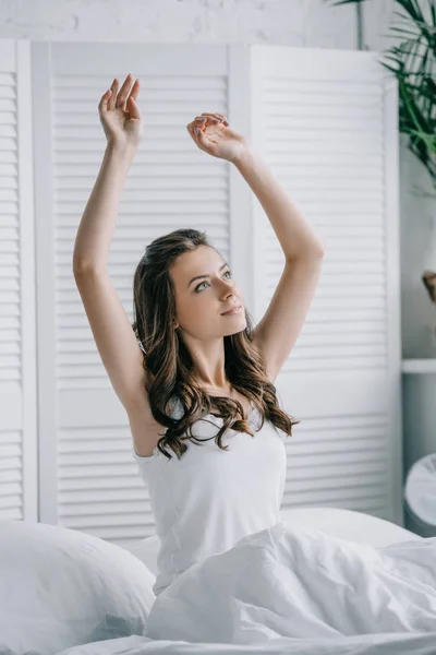 Красивая молодая женщина сидит на кровати и протягивает руки — стоковое фото