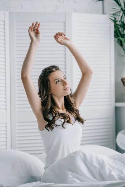 Hermosa joven sentada en la cama y estirando las manos - foto de stock