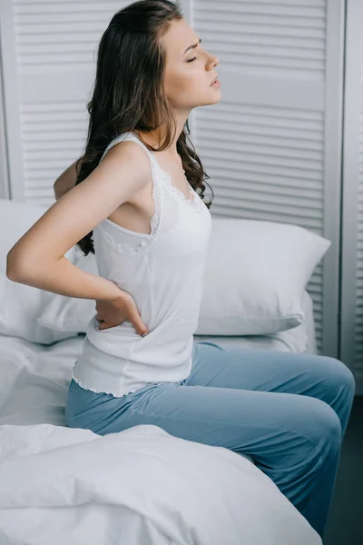Vista lateral de la joven mujer en pijama que sufre de dolor de espalda en la cama - foto de stock