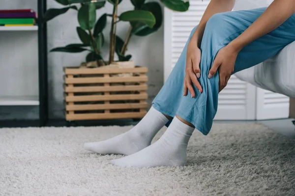 Abgeschnittene Aufnahme einer Frau, die auf dem Bett sitzt und Schmerzen im Bein hat — Stockfoto