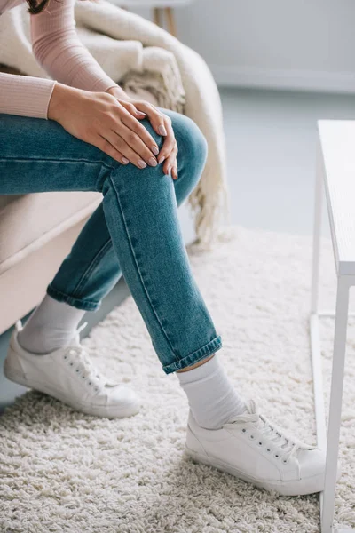 Cropped shot of woman sitting on couch and suffering from pain in knee — Stock Photo