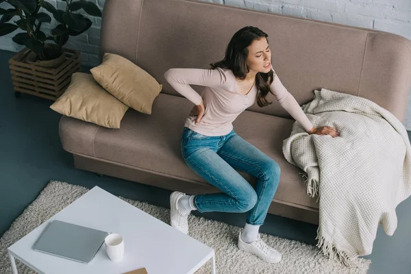 Blick aus der Vogelperspektive auf junge Frau mit Rückenschmerzen auf der heimischen Couch — Stockfoto