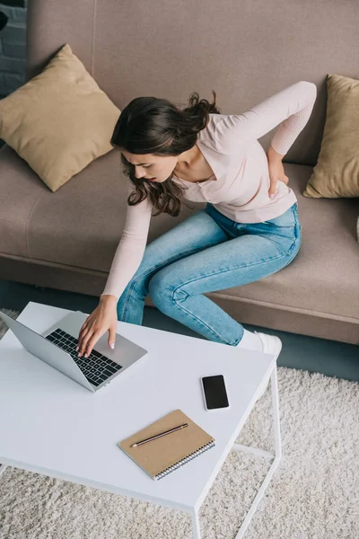 Vista de ángulo alto de la mujer joven con dolor de espalda utilizando el ordenador portátil en casa - foto de stock