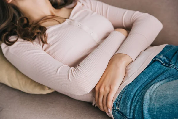 Обрезанный снимок молодой женщины с болью в животе, лежащей на диване — стоковое фото