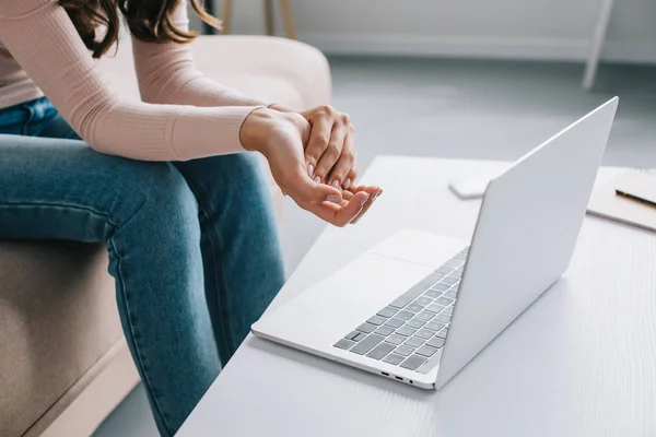 Partial view of woman suffering from pain in hand while using laptop at home — Stock Photo