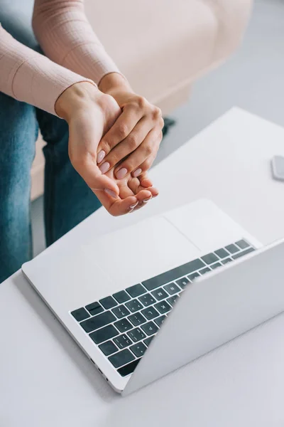 Cropped shot of woman suffering from pain in hand while using laptop — Stock Photo