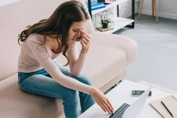 Junge Frau reibt Nasenrücken, während sie zu Hause Laptop benutzt — Stockfoto