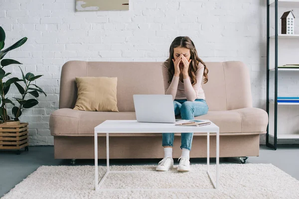 Junge Frau mit Kopfschmerzen reibt Nasenrücken, während sie zu Hause mit Laptop arbeitet — Stockfoto