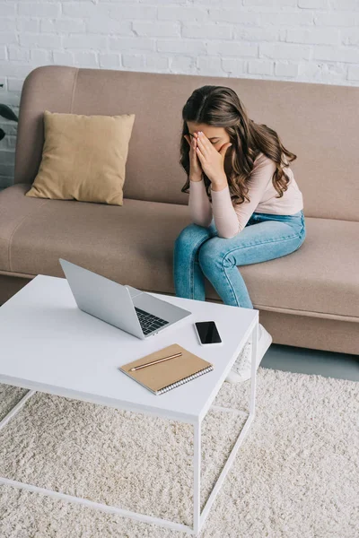 Junge Frau mit Kopfschmerzen sitzt auf Sofa und arbeitet zu Hause mit Laptop — Stockfoto