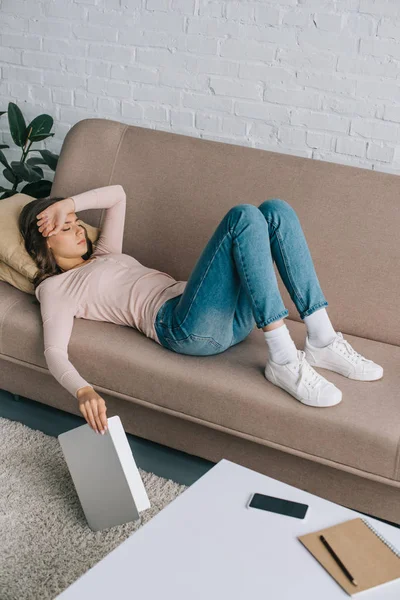 High angle view of young woman with headache lying on sofa and holding laptop — Stock Photo