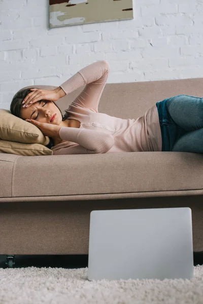Mujer joven con dolor de cabeza tumbada en el sofá en casa - foto de stock