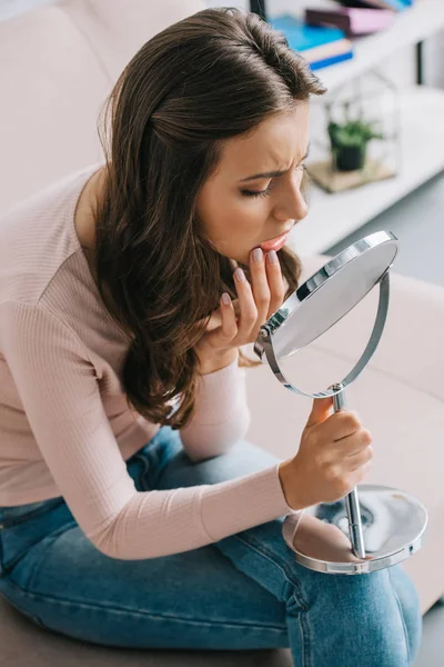 Hochwinkelaufnahme einer jungen Frau mit Zahnschmerzen, die sitzt und in den Spiegel schaut — Stockfoto