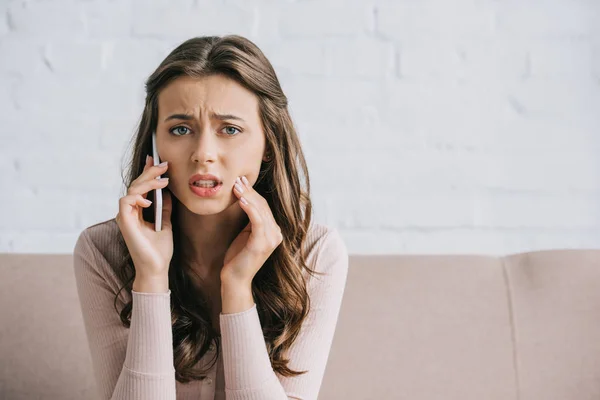 Mujer joven con dolor de muelas hablando por teléfono inteligente y mirando a la cámara — Stock Photo