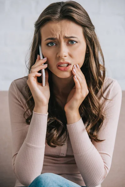 Junge Frau mit Zahnschmerzen spricht mit Smartphone und blickt in Kamera — Stockfoto