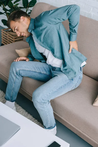 High angle view of man suffering from back pain while sitting on couch — Stock Photo