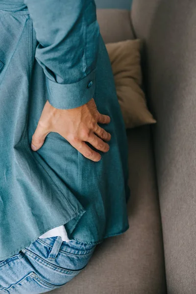 Cropped shot of man sitting on sofa and suffering from back pain — Stock Photo