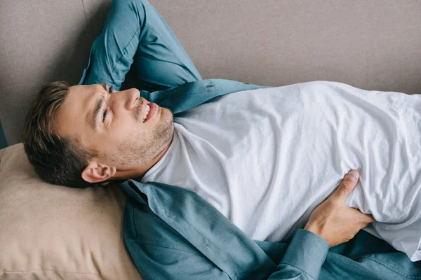 Молодой человек страдает от болей в спине и лежит на диване — стоковое фото