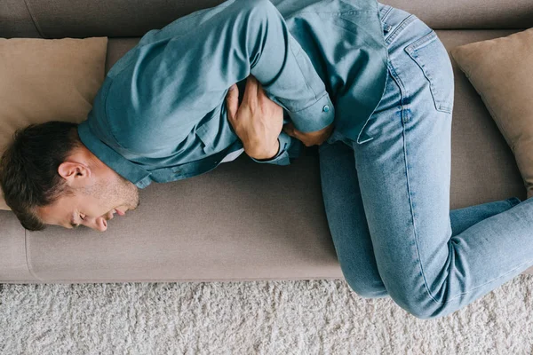 Top view of man lying on sofa and suffering from stomach ache — Stock Photo