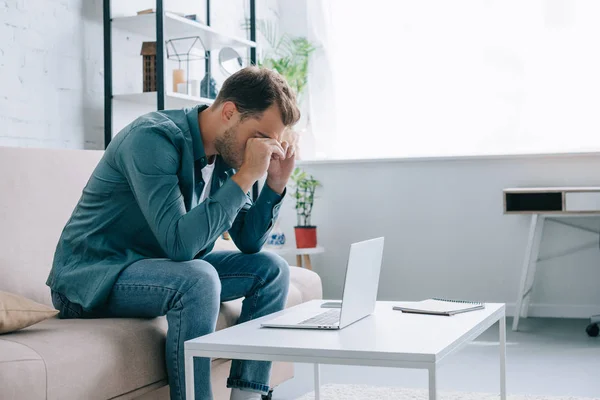 Junger Mann reibt sich die Augen, während er zu Hause mit Laptop arbeitet — Stockfoto