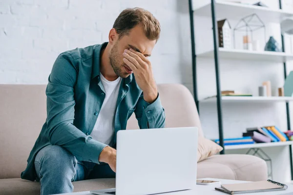 Jeune homme avec douleur dans les yeux en utilisant un ordinateur portable à la maison — Photo de stock