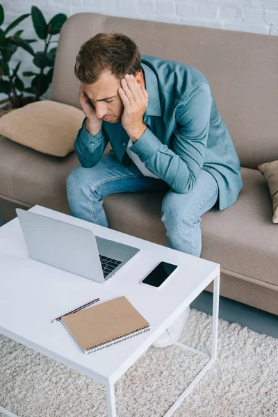 Vue grand angle du jeune homme avec des maux de tête en utilisant un ordinateur portable à la maison — Photo de stock