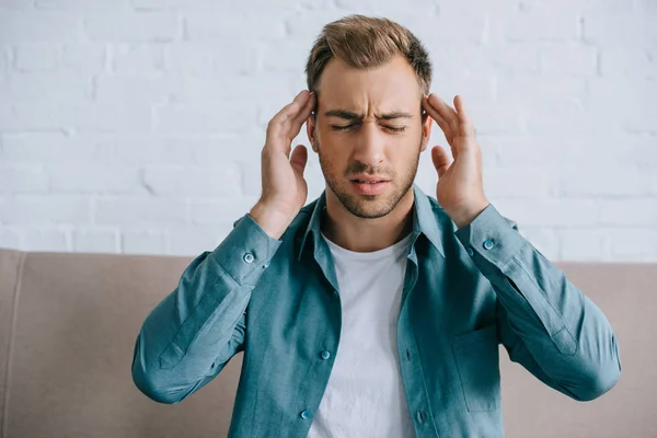 Young man with closed eyes suffering from headache while sitting at home — Stock Photo